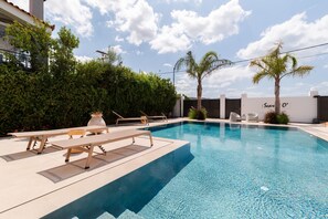 A swimming pool with lounge chairs and a palm tree, surrounded by greenery and a building with a sign that reads "Seur O'". - Scarlet O in Thimari (Saronikos)