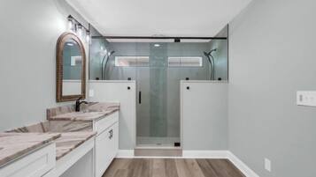 A bathroom with a shower, a vanity with a mirror, and a marble countertop.