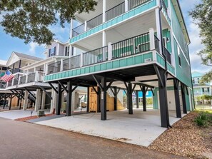 A multi-story building with balconies, a covered entrance, and a flag. - Stunning 4-Bed with Ocean View in Ocean Lakes Golf Cart | Site 1199 (Myrtle Beach)