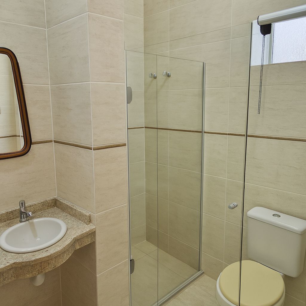 A bathroom with a glass shower enclosure, a toilet, and a sink with a mirror above it.