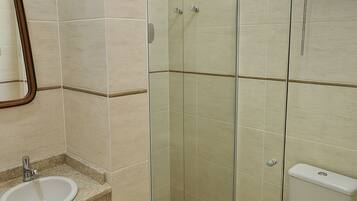 A bathroom with a glass shower enclosure, a toilet, and a sink with a mirror above it.