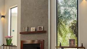 A spacious living room with a fireplace, a large window with a view of palm trees, and a modern pendant light. - Luxury House in Gated Community in Metropolitan Area (Mogi das Cruzes)