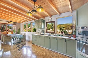 Una cocina amplia con vigas de madera, armarios verdes, suelo de baldosas y vistas al exterior.