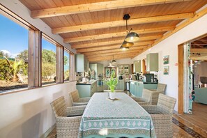 A dining area with wicker furniture, a table with a patterned tablecloth, and a view of the kitchen and garden. - Paris Room - Naturist B&B for Couples (Monte da Charneca)