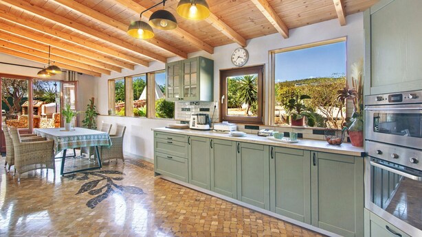 A spacious kitchen with wooden beams, green cabinets, a tiled floor, and a view of the outdoors. - Sevilha Room – Naturist B&B for Couples (Monte da Charneca)