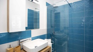 A modern bathroom with a white sink, a glass shower enclosure, and blue-tiled walls. - L'Arca di Noè (Sorrento)