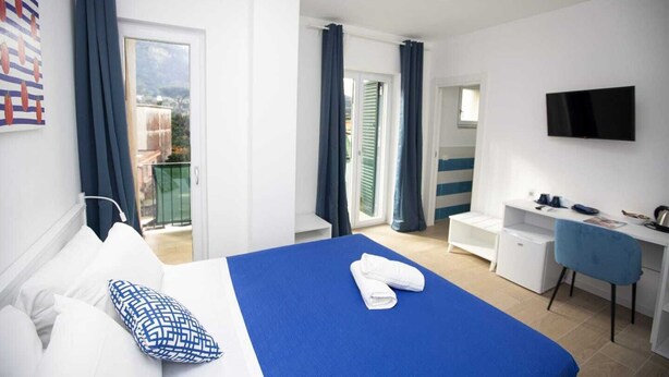 A hotel room with a bed, a desk, a TV, and a balcony with curtains. - L'Arca di Noè (Sorrento)