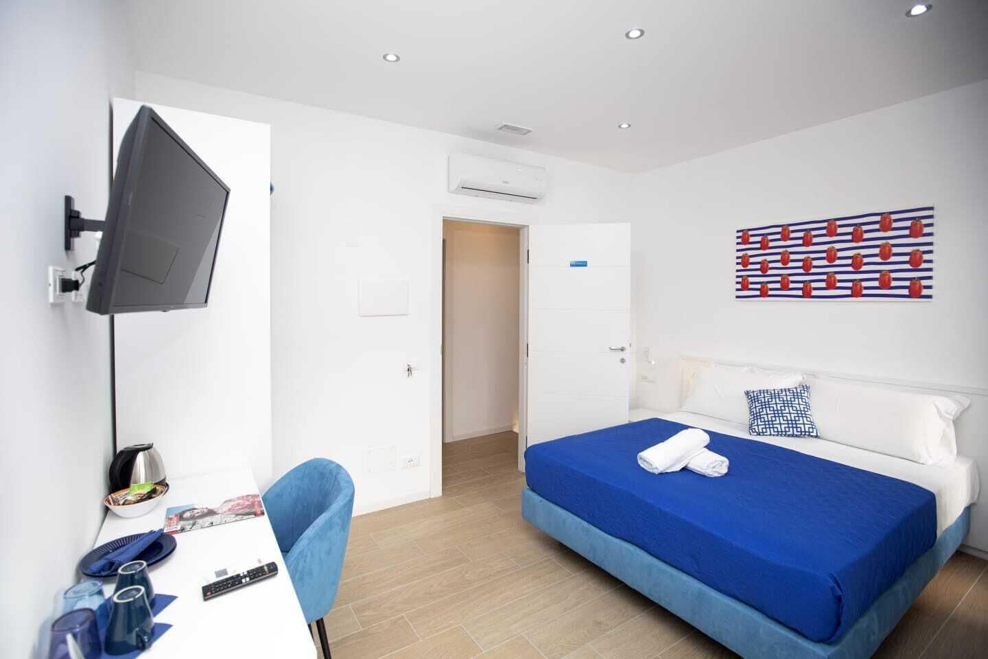 A hotel room with a bed, a desk with a chair, a TV mounted on the wall, and a window.