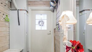 Hotellihuone, jossa on puulattia, valkoinen ovi, jossa on ikkuna, pieni penkki, peili ja punakukkainen kasvi.