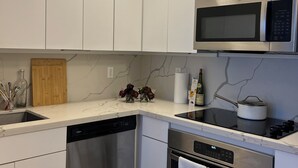 A modern kitchen with white cabinets, a stainless steel microwave, a dishwasher, an oven, and a countertop with a vase of flowers. - Beautiful, cozy boho chic apartment in the Heart of South Beach, Miami (Miami Beach)