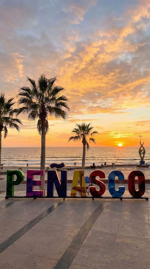 Eine Strandansicht mit Palmen und dem Wort 'PENASCO', das in bunten Buchstaben geschrieben steht.