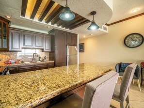 Eine Küche mit Granit-Arbeitsplatten, dunklen Holzschränken, Edelstahlgeräten, Pendelleuchten und einer Wanduhr.
