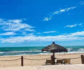 A beach with a thatched umbrella, two chairs, and a chain barrier.