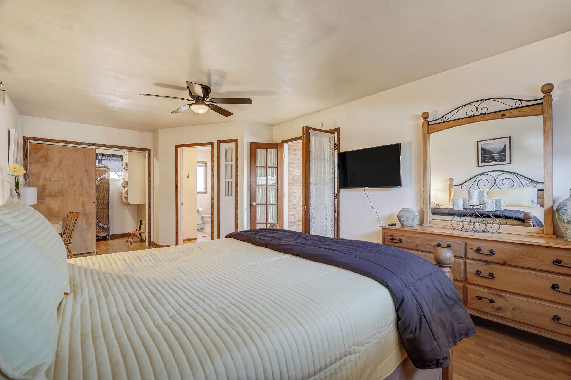 A bedroom with a bed, a dresser, a mirror, a ceiling fan, and a TV.