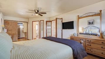 A bedroom with a bed, a dresser, a mirror, a ceiling fan, and a TV.