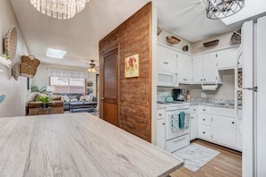 Une cuisine moderne avec des meubles blancs, une table à manger en bois et un ventilateur de plafond.