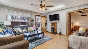 A living room with a sofa, coffee table, and chairs, a TV, and a ceiling fan.