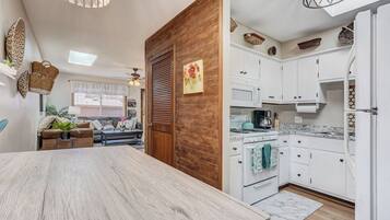 A modern kitchen with white cabinets, a stove, and a microwave. There is a dining area with a wooden table and a sofa.