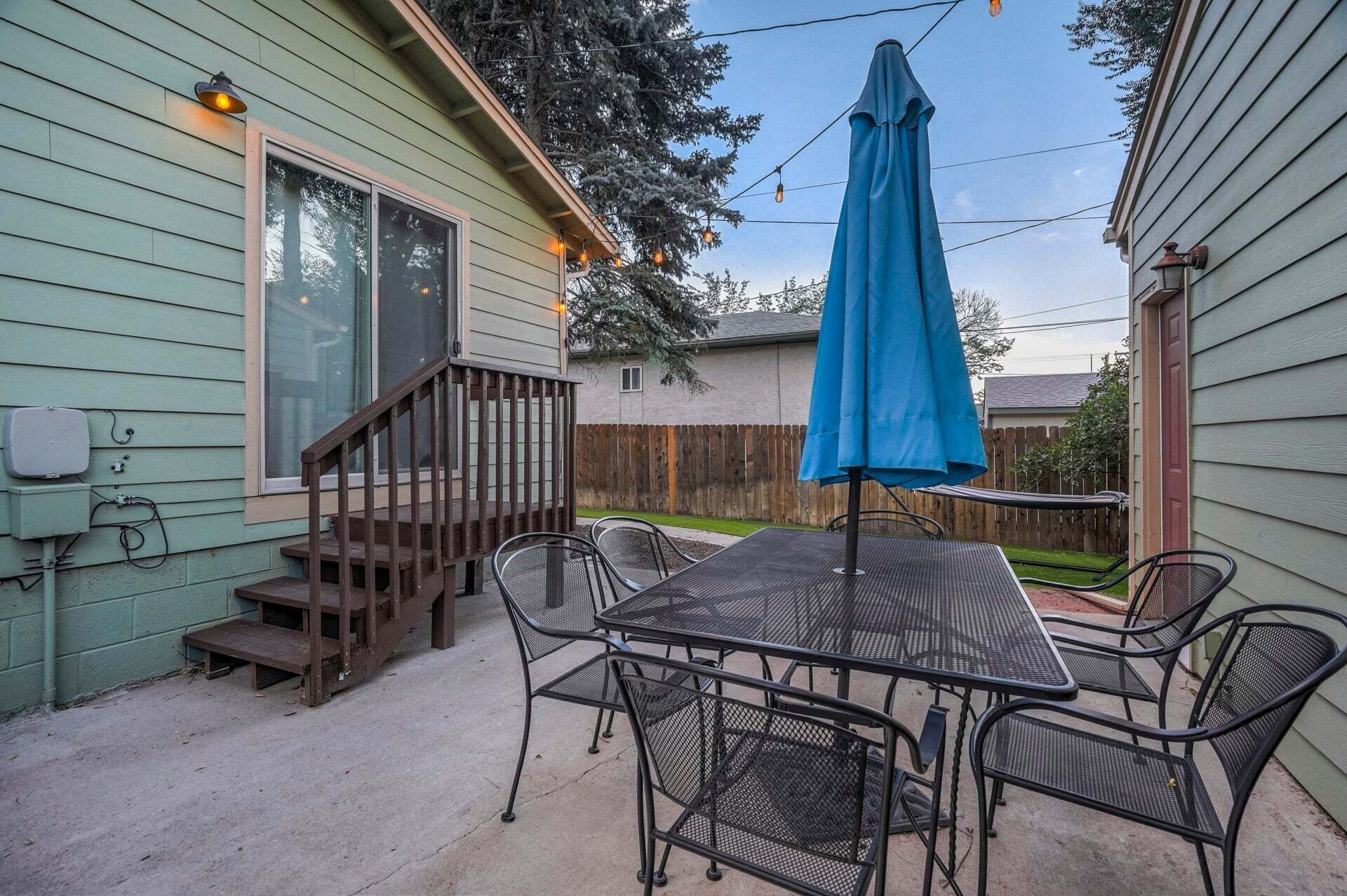 Un patio con una mesa, sillas y una sombrilla azul, además de un deck de madera.