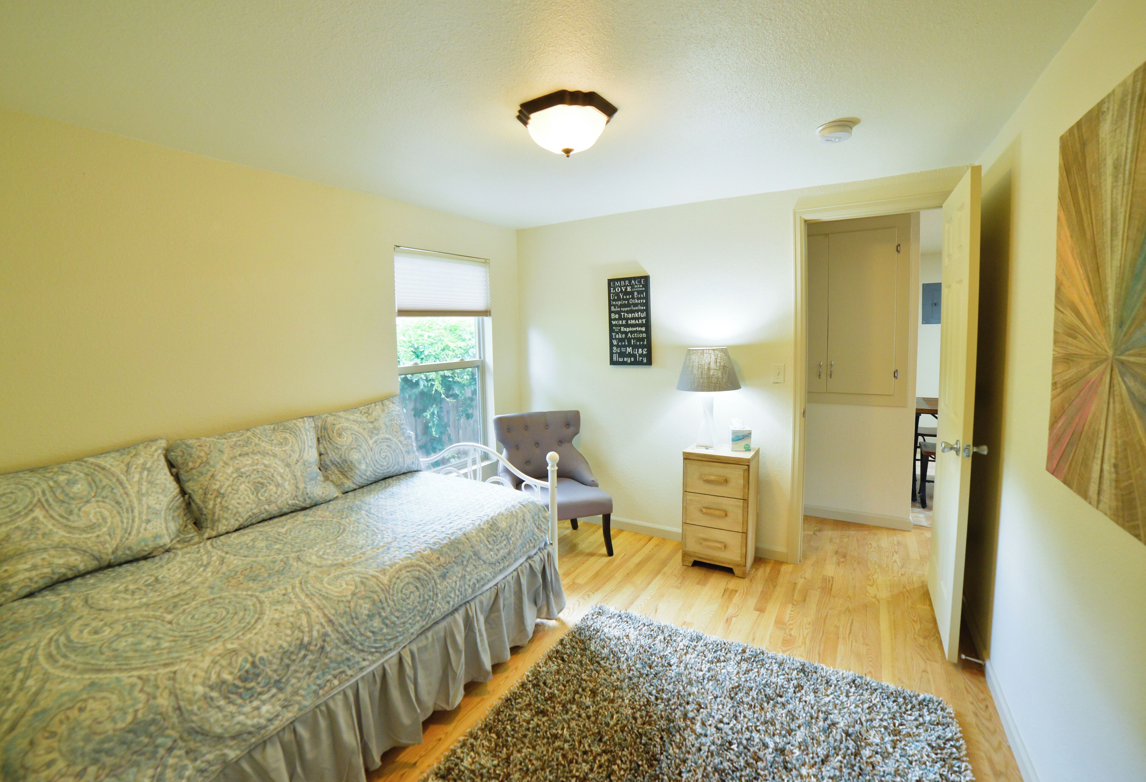 A bedroom with a bed, a chair, a nightstand, and a door leading to another room.