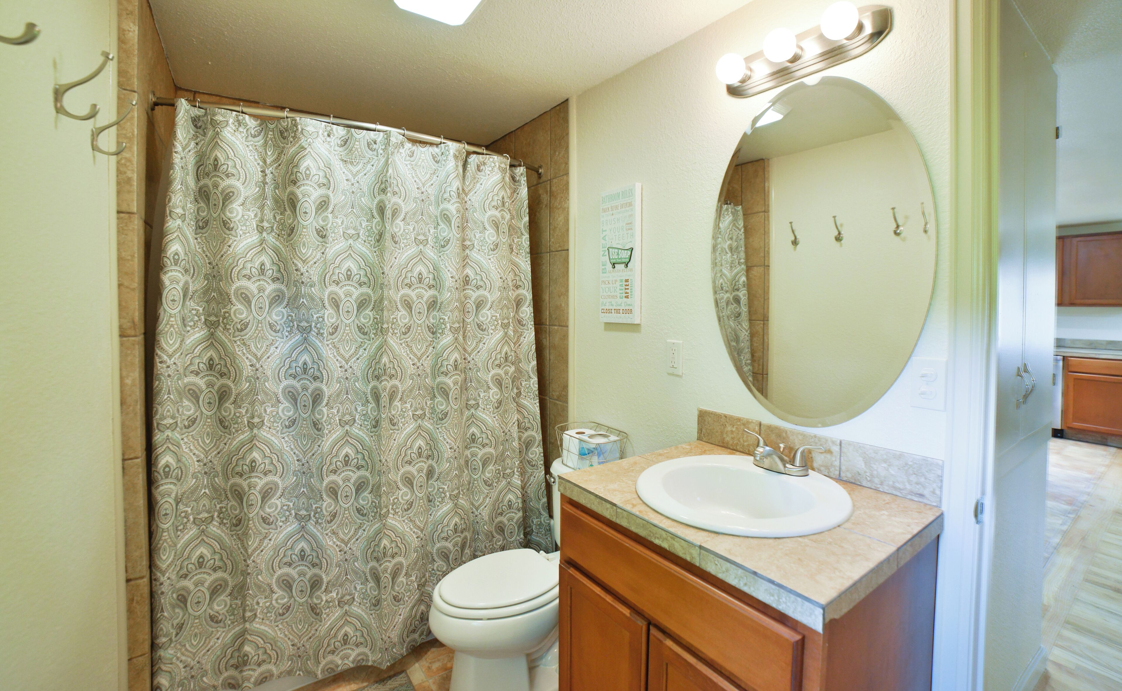 Un bagno con tenda da doccia decorata, un water, un lavandino con specchio sopra e un armadietto.