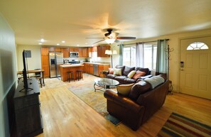 A spacious living room with a leather sofa, a coffee table, and a dining area with wooden cabinets and a refrigerator. - 1014b Swope (Colorado Springs)