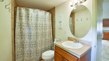 A bathroom with a patterned shower curtain, a toilet, a sink with a mirror, and a sign on the wall.