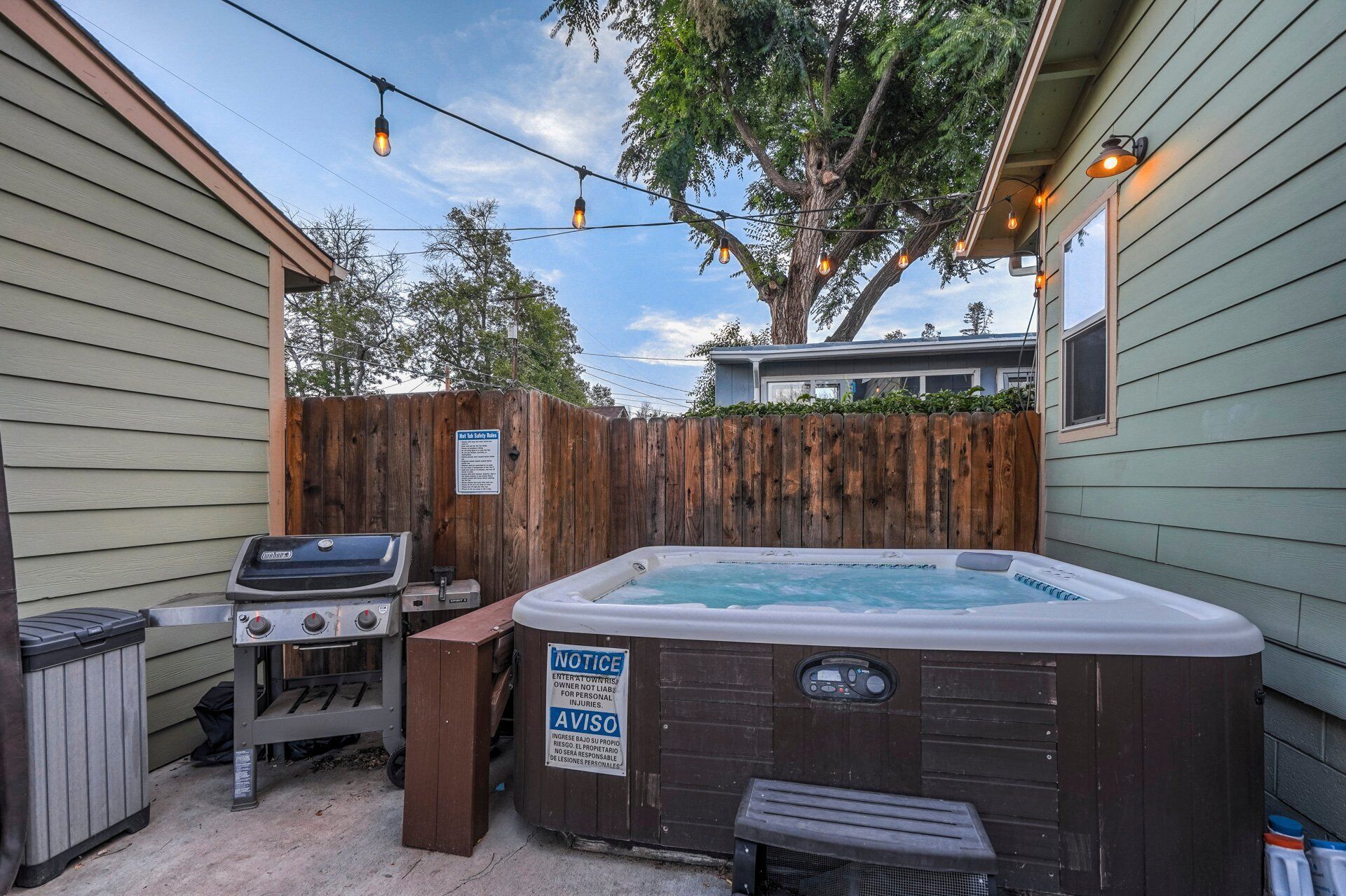 A backyard with a hot tub, barbecue grill, and a wooden fence.