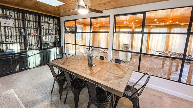 A dining area with a large wooden table, black chairs, and a ceiling fan. There is a bookshelf with various items and large windows with curtains. - 1625 E Cache La Poudre (Colorado Springs)
