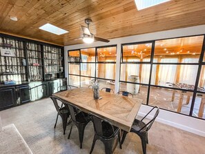 A dining area with a large wooden table, black chairs, and a ceiling fan. There is a bookshelf with various items and large windows with curtains. - 1625 E Cache La Poudre (Colorado Springs)