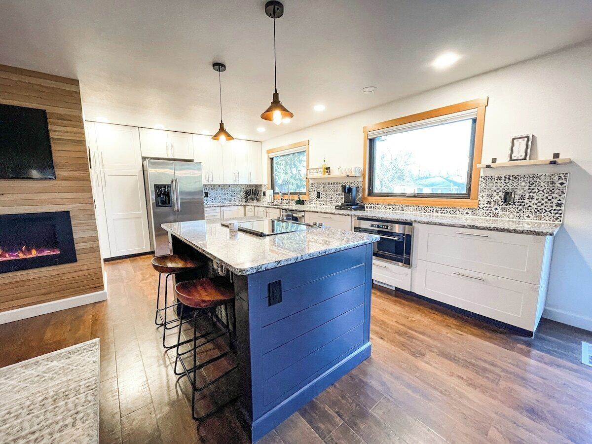 A modern kitchen with a central island, bar stools, a built-in oven, and a large window providing natural light.
