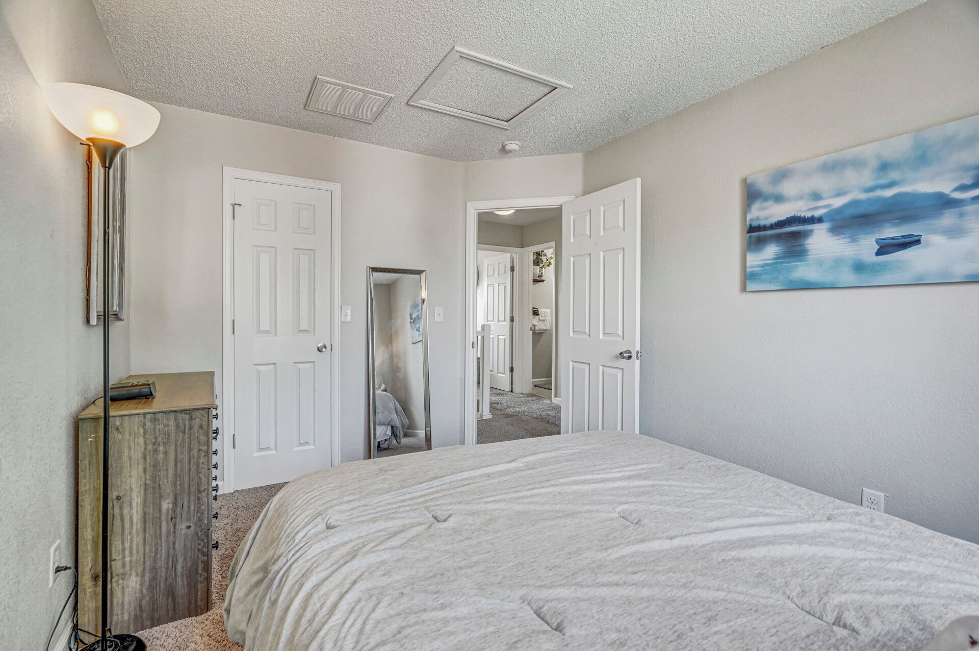 A bedroom with a large bed, a floor lamp, and a painting of a lake.