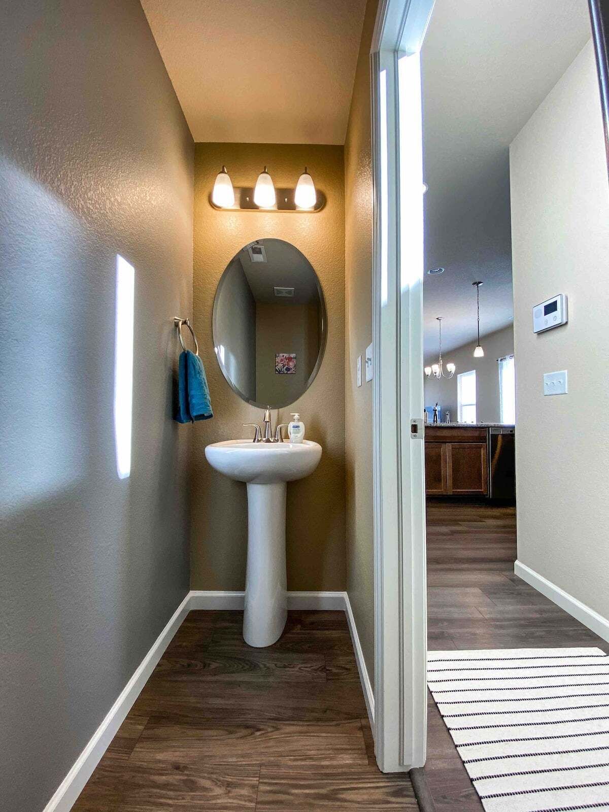 Un baño con lavamanos pedestal, un espejo redondo y un perchero para toallas.