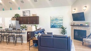 Un salon moderne avec un canapé bleu foncé, une cheminée et un coin cuisine doté de meubles sombres et d’un grand îlot central.