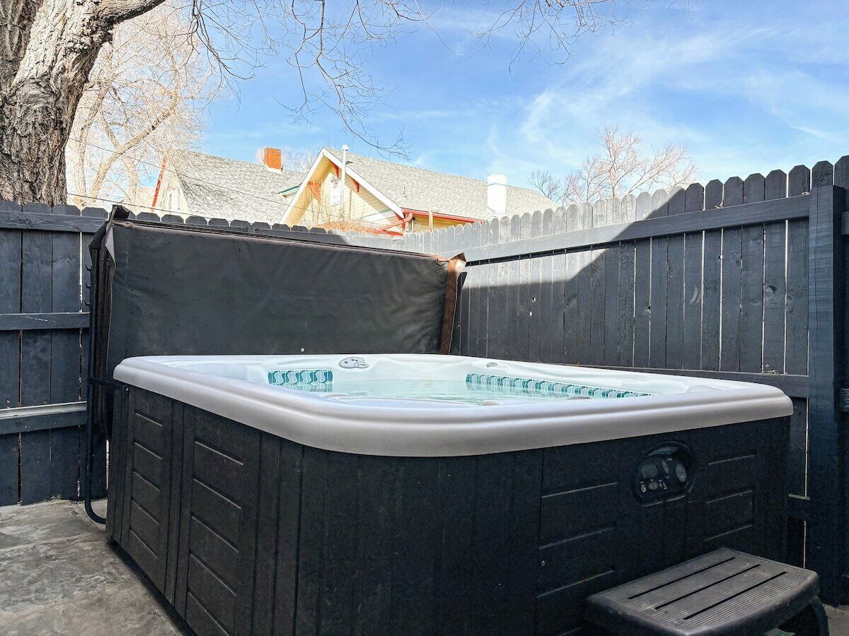 A hot tub in a backyard with a wooden fence and a house in the background.
