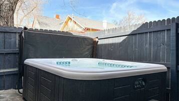 A hot tub in a backyard with a wooden fence and a house in the background.
