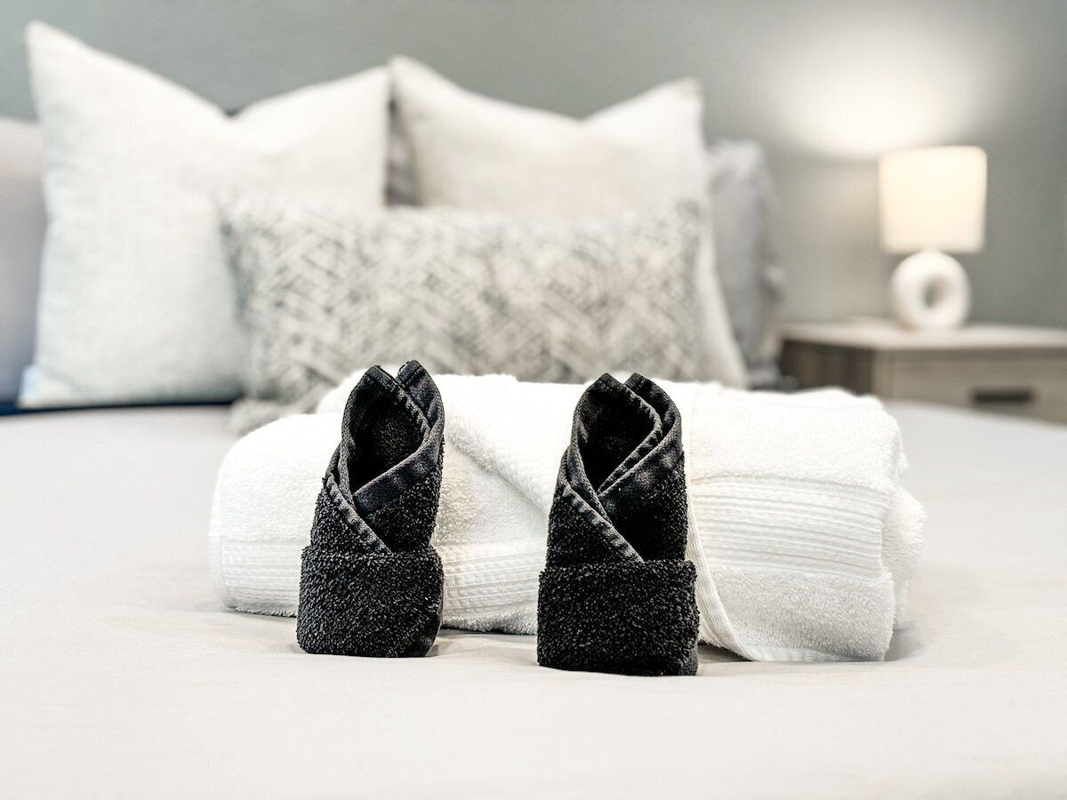 Una cama bien hecha con sábanas blancas, un par de zapatillas negras y una toalla blanca.