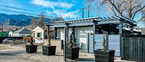 A modern building with a covered patio area, surrounded by a gravel driveway and potted plants.
