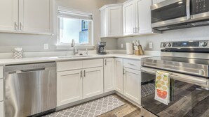 A modern kitchen with white cabinetry, stainless steel appliances, and a patterned rug. - 5370 N Union Unit101 (Colorado Springs)