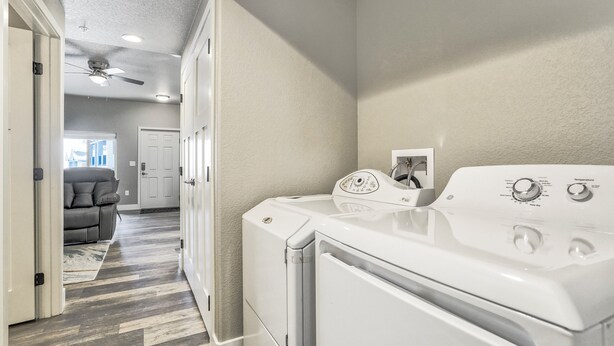 A laundry room with a front-loading washer and dryer, a ceiling fan, and a hallway leading to a living area with a couch and a door. - 5370 N Union Unit101 (Colorado Springs)