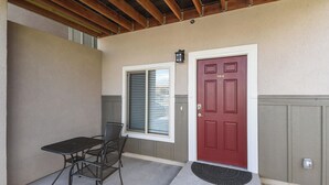 A covered patio with a table and chairs, a red door, and a window with blinds. - 5370 N Union Unit101 (Colorado Springs)