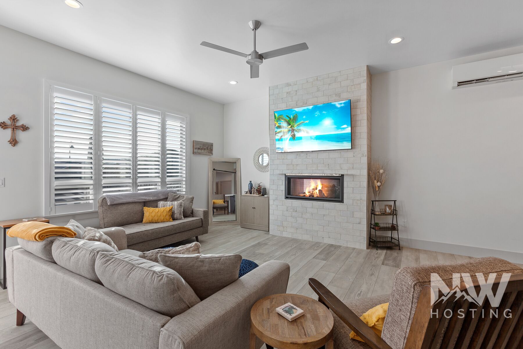 A modern living room with a grey sofa, a fireplace, and a TV mounted on a brick wall.