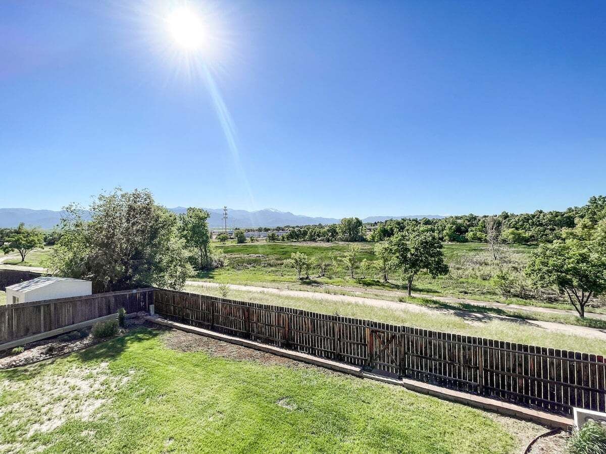 A fenced outdoor area with a grassy lawn, trees, and a clear sky.