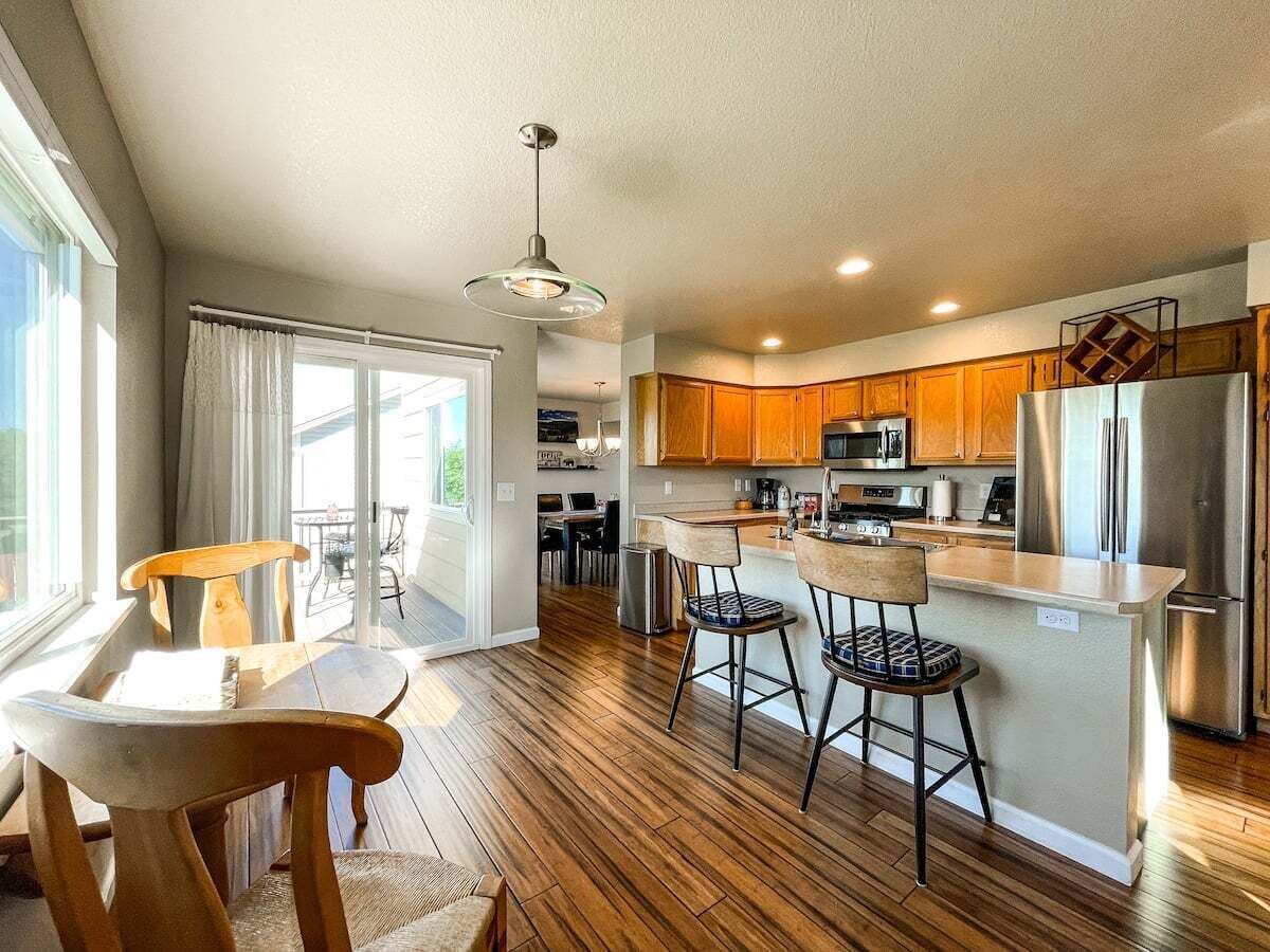 A modern kitchen with wooden cabinets, a stainless steel refrigerator, and a bar area with stools. - 1040 Pond Side (Colorado Springs)
