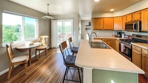 A modern kitchen with wooden cabinets, a large island, and a dining area with a view. - 1040 Pond Side (Colorado Springs)