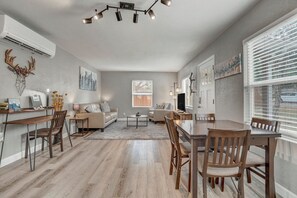 A spacious living room with a dining area, a fireplace, and a large window with blinds. - 1313 Cooper (Colorado Springs)