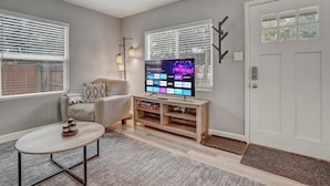 A living room with a flat-screen TV, a sofa, a coffee table, and a wooden entertainment unit. - 1313 Cooper (Colorado Springs)