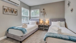 A hotel room with two beds, a small table with lamps, and decorative wall art. - 1313 Cooper (Colorado Springs)