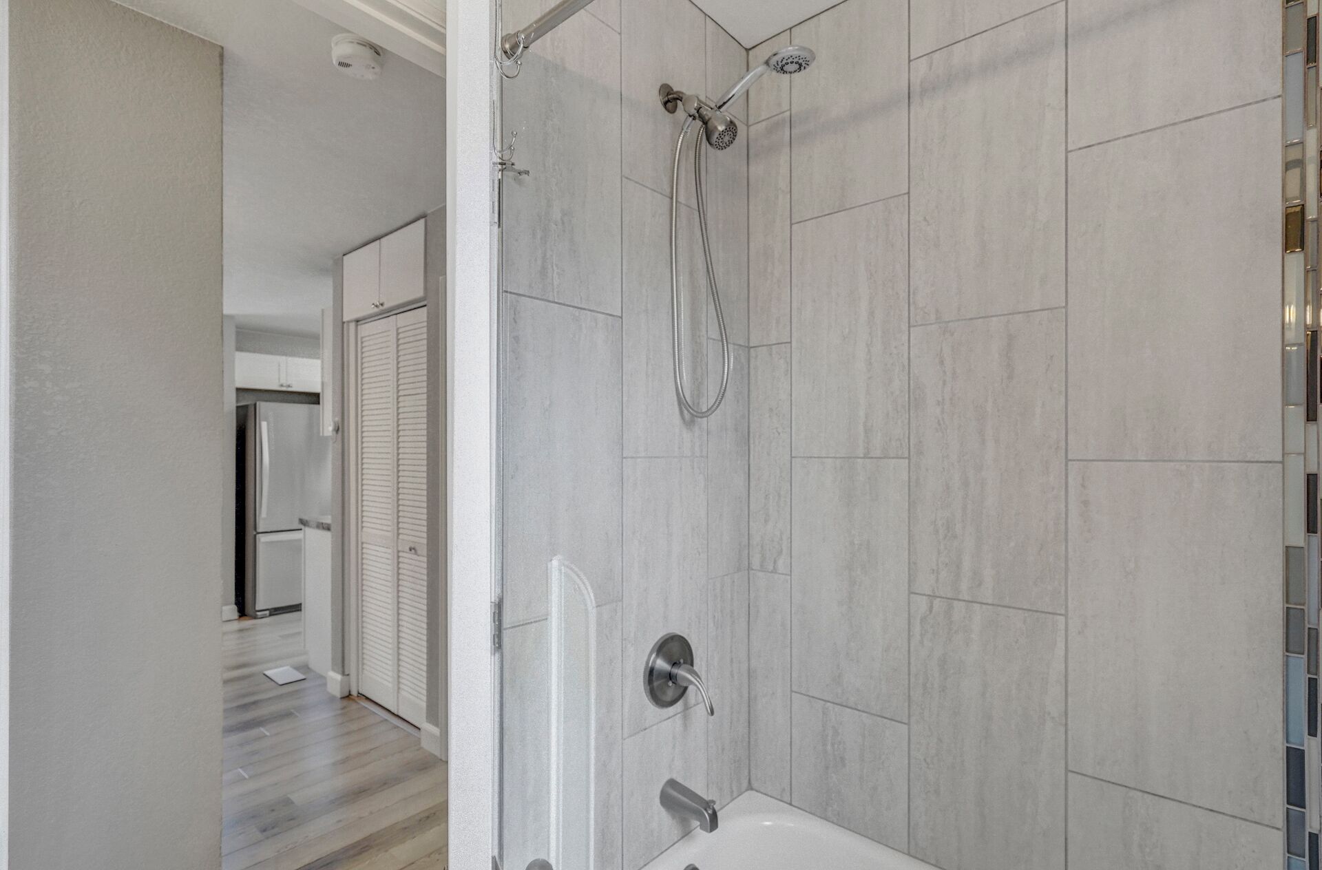 Une salle de bain moderne avec une douche, des murs carrelés et une porte visible donnant sur une autre pièce.
