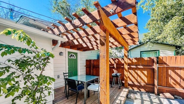Un patio in legno con una pergola, un tavolo e sedie, e una porta verde.